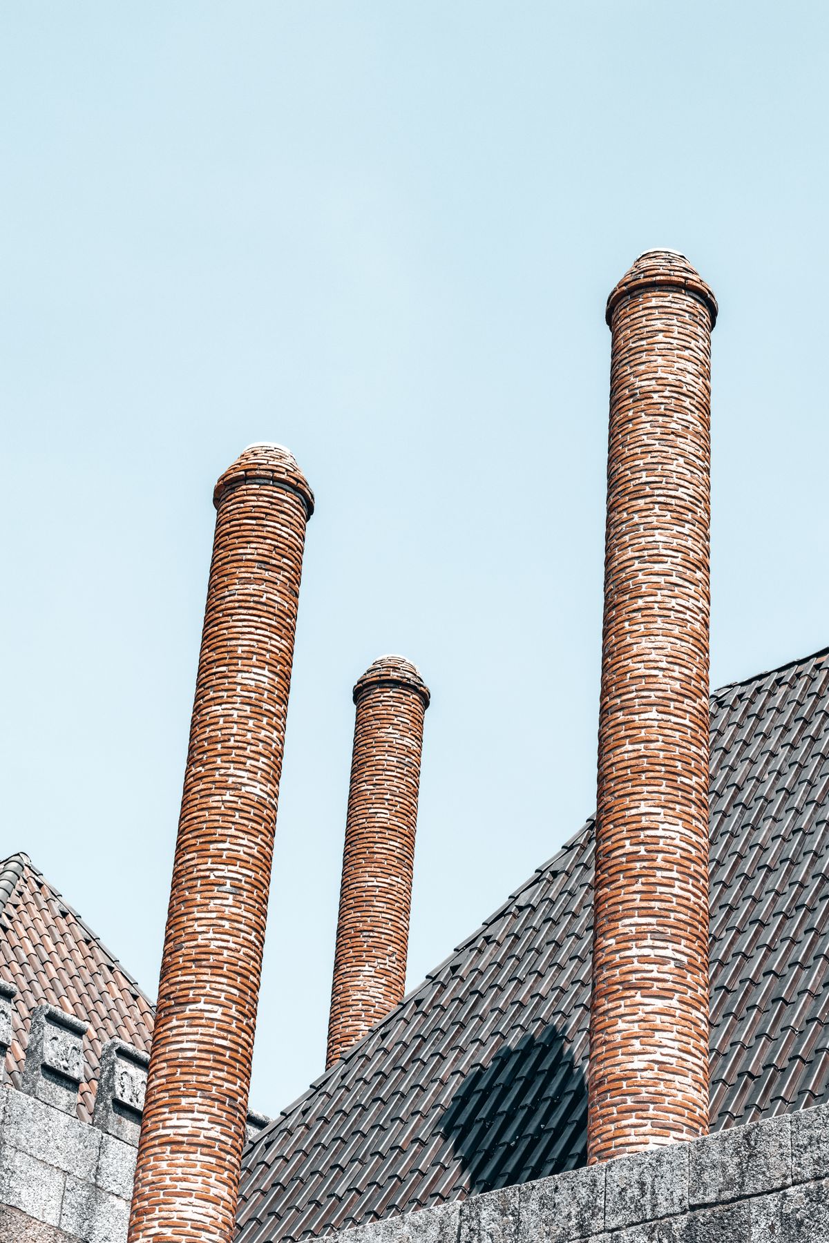 Three tall round brick chimney stacks rising above a tiled roof into a clear sky