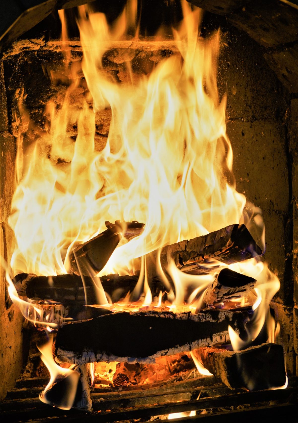 Close-up of bright orange flames and glowing embers around burning logs inside a brick firebox