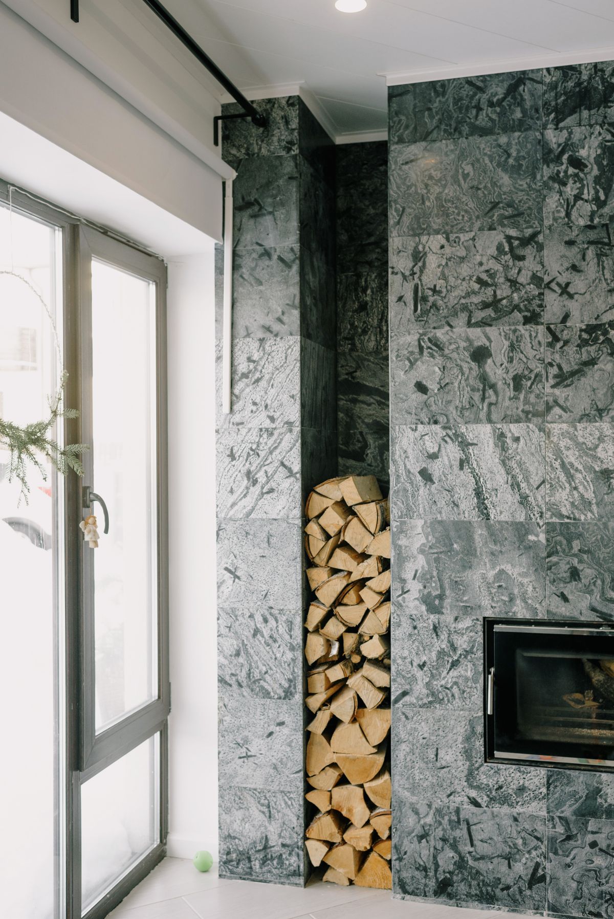 Modern grey stone fireplace with an inset firebox and a tall niche stacked with split firewood