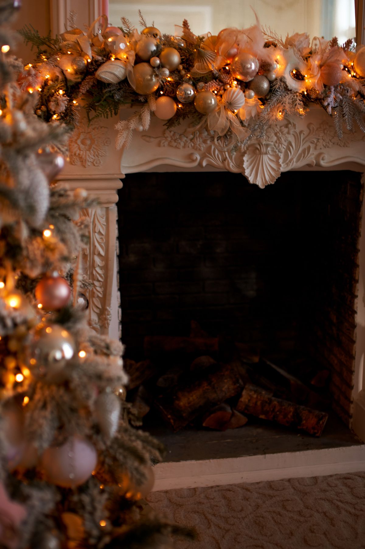 Ornate white fireplace mantel decorated with a festive garland above an unlit firebox stacked with logs